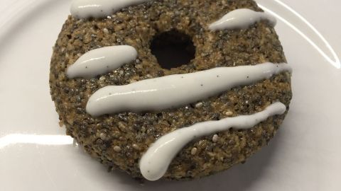 Ein Chia-Donut mit einer glänzenden, weißen Zitronen-Kokos-Creme-Dekoration liegt auf einem weißen Teller.