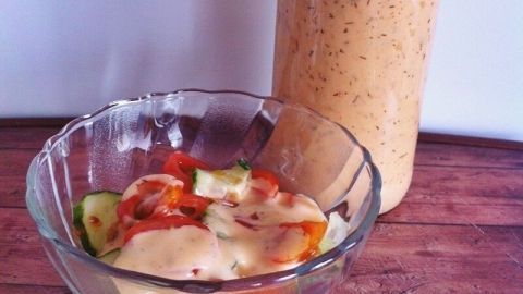 Eine Flasche mit selbstgemachtem French Dressing steht neben einer Schüssel, die mit frischem Gemüse gefüllt ist.