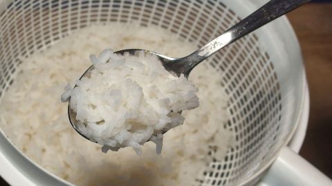 Ein Löffel mit gekochtem Reis wird aus einem Sieb gehoben, während er in einer modernen Küchenumgebung steht.