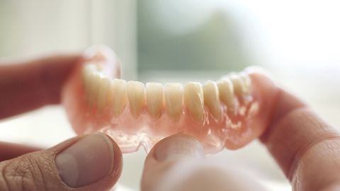 Eine Hand hält eine Zahnprothese, während sie zur Reinigung der Verfärbungen in sanfter Beleuchtung betrachtet wird.