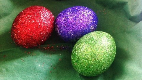 Glitzernde Ostereier in Rot, Lila und Grün liegen auf einem grünen Tuch und sorgen für festliche Stimmung.