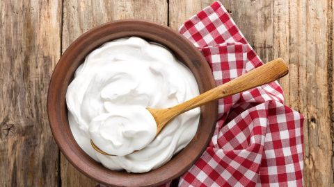 Eine Schüssel mit Joghurt steht auf einem Holztisch, während ein Holzlöffel bereit ist, ihn für Salatsoßen zu verwenden.