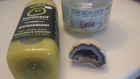 Eine Flasche antioxidierender Smoothie und ein Glas Kokosöl liegen auf einer hellen Oberfläche, umgeben von dem bunten Umfeld.