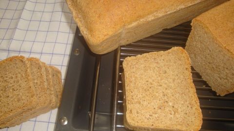 Frisch gebackenes Brot liegt auf einem Gitter, während eine Scheibe neben einem Laib platziert ist.