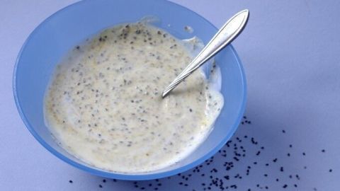 Ein blauer Schüssel mit Power-Joghurt, der cremig aussieht und mit Chia-Samen sowie Gewürzen verfeinert ist, steht auf einem hellen Tisch.