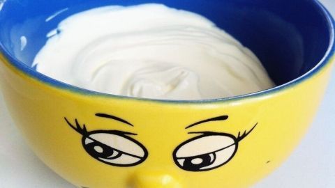 Eine bunte Schüssel mit einem lachenden Gesicht enthält cremigen Joghurt, bereit zum Backen und Kochen in einer hellen Küche.