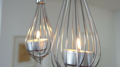 Teelichter leuchten im dekorativen Schneebesen, der elegant von der Decke hängt und eine moderne Atmosphäre schafft.