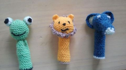 Häkel-Fingerpuppen zeigen eine grüne Frosch-, eine gelbe Löwen- und eine blaue Elefantenfigur auf einem Tisch.