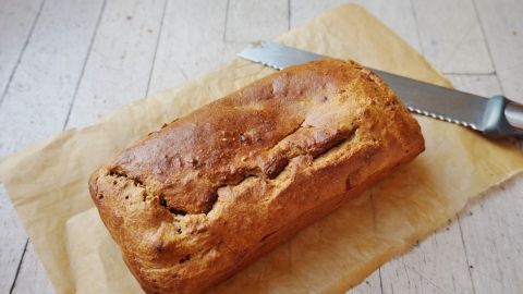 Ein frisch gebackener Bananenkuchen liegt auf Pergamentpapier, neben einem Schneidemesser in einer hellen Umgebung.