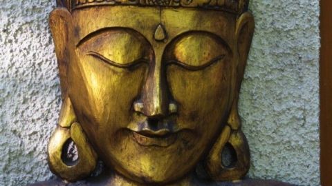 Ein goldener Buddha mit geschlossenen Augen strahlt Ruhe aus, vor einer strukturierten grauen Wand.