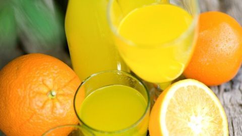 Gläser mit frischer Orangen-Zitronen-Limonade stehen auf einem Holzbrett, umgeben von Orangen und grünen Blättern.