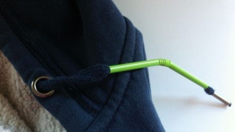Eine grüne Schnur zieht sich durch die Öffnung eines dunkelblauen Pullovers, der sich auf einer hellen Oberfläche befindet.