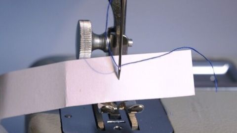 Eine Nähmaschinennadel durchstößt ein Stück Stoff, während der Faden durch das Einfädelloch geführt wird.