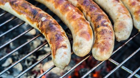 Gegrillte Würstchen liegen auf einem Rost über glühender Kohle und zeigen appetitliche Grillspuren, ideal für ein BBQ.