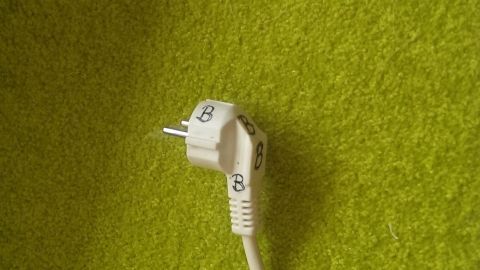 Ein weißer Stecker liegt auf einem grünen Teppich und ist nicht mit einem Gerät verbunden, was Fragen zum Bügeleisen aufwirft.
