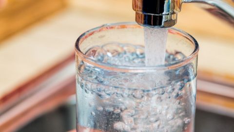 Ein Glas wird unter einen Wasserhahn gehalten, während sprudelndes Wasser hineinläuft, ideal gegen Schluckauf.