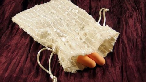 Weiße Schaumstoff-Ohrstöpsel liegen in einem durchsichtigen Beutel auf einem rot-violetten Untergrund, bereit zum Reinigen.