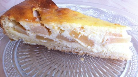 Ein Stück Apfel-Quarkkuchen liegt auf einem dekorativen Glasteller, umgeben von einer hellen, natürlichen Umgebung.