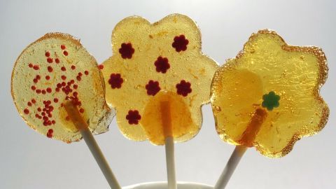 Bunte Lollies stehen in einem hellblauen Becher und erfreuen mit fröhlichen, süßen Formen und bunten Streuseln.