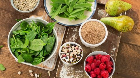 Schalen mit frischen Zutaten wie Spinat, Himbeeren und Körnern liegen auf einem Holzbrett in einer Küche.