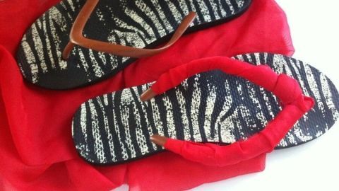 Bunte Flip-Flops mit Zebramuster liegen auf einem roten Tuch, bereit für eine kreative Verschönerung.