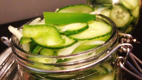 Zwei Gläser mit frisch geschnittenem Gurkensalat stehen auf einer dunklen Oberfläche und sind bereit zur Zubereitung.
