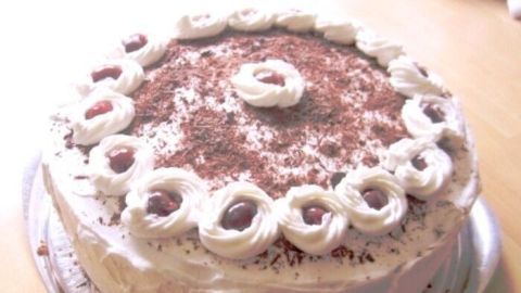 Eine Schwarzwälder Kirschtorte steht auf einem silbernen Teller, mit Sahne und Kirschen dekoriert, in einem hellen Raum.