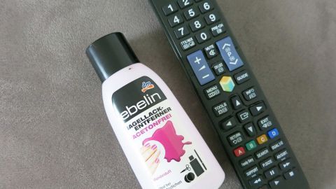 Flecken von Tipp-Ex auf Taschenrechner oder Fernbedienung mit Nagellackentferner entfernen. Einfach ein Wattepad oder ein Zewatuch mit dem Nagellackentferner anfeuchten und über den Fleck reiben. Ein Nagellackentferner steht neben einer Fernbedienung auf einem grauen Untergrund, bereit, Tipp-Ex-Flecken zu entfernen.