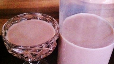 Ein Glas Likör aus Kinderschokolade steht neben einer Flasche mit einer ähnlichen, hellbraunen Flüssigkeit.
