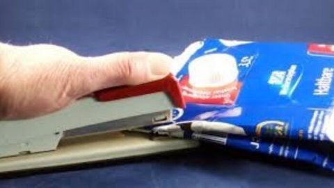 Eine Hand verwendet einen Tacker, um einen Tetrapak zu verschließen und spart Platz im Mülleimer.