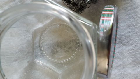 Ein hübscher silberner Schraubglasdeckel liegt auf einem klaren Glasbehälter, der auf einer neutralen Unterlage platziert ist.