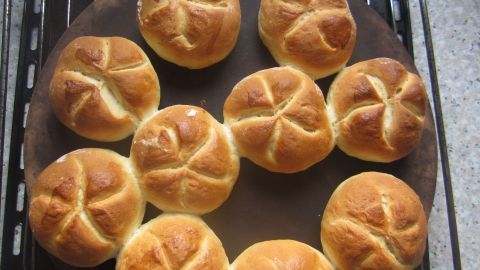 Kaisersemmeln liegen frisch gebacken auf einem runden Blech und strahlen eine goldbraune Farbe aus.