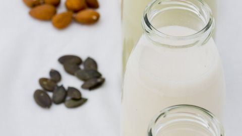 Glasflaschen mit pflanzlicher Milch stehen nebeneinander, umgeben von Nüssen und Samen, die verschiedene Alternativen zeigen.