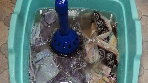 Ein blauer Pümpel steht in einem Eimer mit Wasser und Wäsche, um diese zu reinigen und zu entlüften.