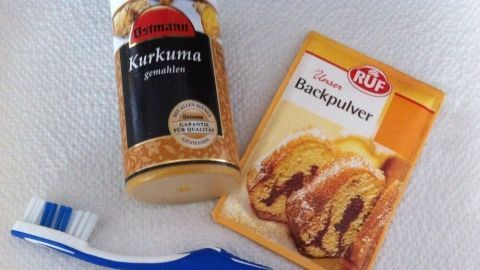 Ein Zahnbürste liegt neben einer Kurkuma-Packung und einem Beutel Backpulver, bereit für die Anwendung zur Zahnaufhellung.