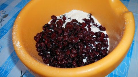 In einer orangefarbenen Schüssel liegen Cranberries und Mehl, bereit zur Zubereitung eines Bananen-Möhren-Cranberry-Kuchens.