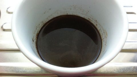 Ein weißer Becher mit dunklem Inhalt steht auf einer Metalloberfläche, bereit für die Anwendung einer effektiven Haarkur.