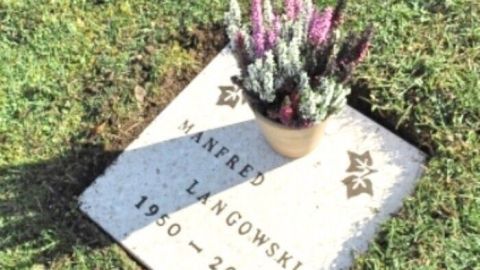 Grabplatte zeigt den Namen "Manfred Langowski, 1950-2008" mit einem Topf violetter Heidepflanzen auf grünem Gras.