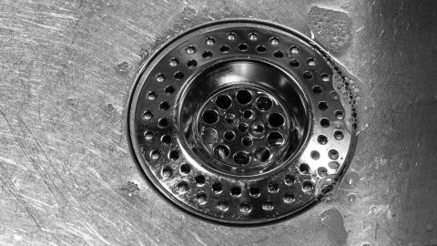 Ein Abfluss im Waschbecken zeigt ein verstopftes Sieb, das auf die Notwendigkeit hinweist, den Abfluss freizuspülen.