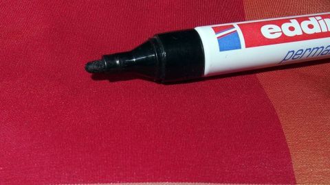 Ein Edding-Marker liegt auf einem rot-gestreiften Polstermöbel, während Oxi Clean zur Fleckentfernung eingesetzt wird.