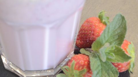 Ein milchiger Erdbeer-Minz-Milchshake steht in einem Glas, umgeben von frischen Erdbeeren und Minzblättern auf einem dunklen Hintergrund.