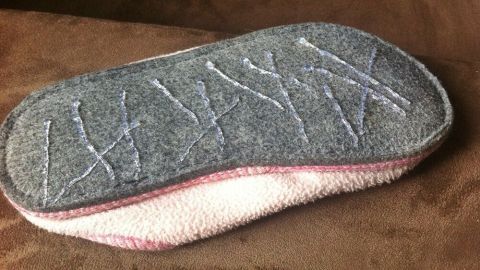 Eine graue Pantolette mit rutschfester Sohle liegt auf einem braunen Untergrund, ideal für das Andocken von Anti Rutsch Hausschuhen.