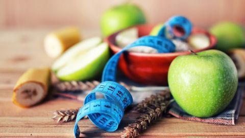 Grüne Äpfel und eine Schüssel mit Joghurt stehen auf einem Holztablett, umgeben von Maßband und einer Banane, als Teil der KFZ-Diät.