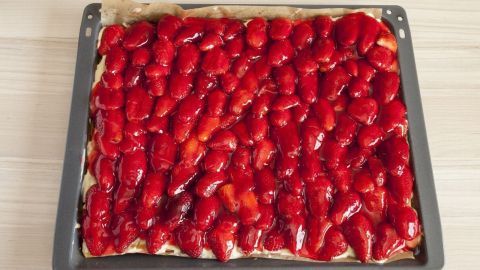Ein marmorierter Erdbeerkuchen auf einem Blech, bedeckt mit glänzenden, roten Erdbeeren, steht auf einer hellen Arbeitsfläche.