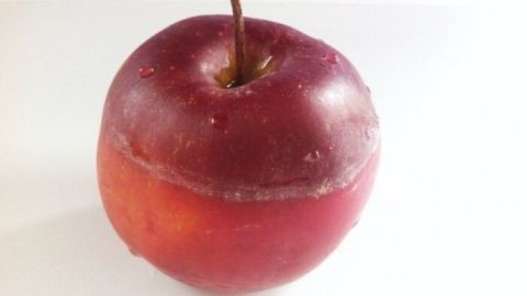 Ein glänzender, roter Apfel mit einer Wachsschicht liegt auf einem weißen Tisch. Er sieht frisch und ansprechend aus.