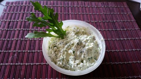 Eine cremige Feta-Rucola-Creme wird in einer Schale präsentiert, umgeben von einem strukturierten Untergrund.