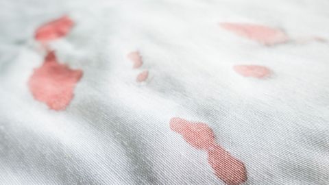 Blutfleck auf weißem Stoffsofa mit Schimmelentferner (Chlor) entfernen. Ein weißes Stoffsofa mit frischen Blutflecken zeigt das Problem, das beim Reinigen behandelt werden muss.