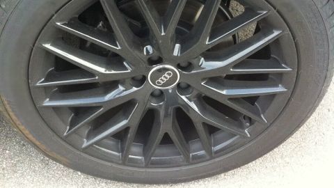 Ein schwarzer Autoreifen mit sportlichem Felgendesign steht auf einer asphaltieren Oberfläche und wartet auf die nächste Fahrt.