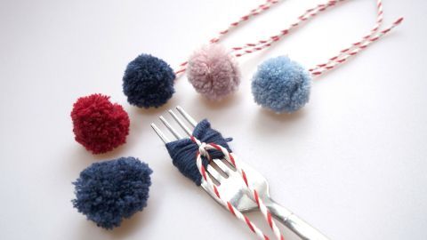 Mini PomPoms aus Wolle liegen auf einem Tisch, während eine Gabel benutzt wird, um sie zu formen und zu binden.