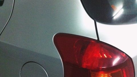 Ein silbernes Auto steht in einer Garage. Der Heckbereich wird gereinigt und gepflegt, sichtbar unter künstlichem Licht.